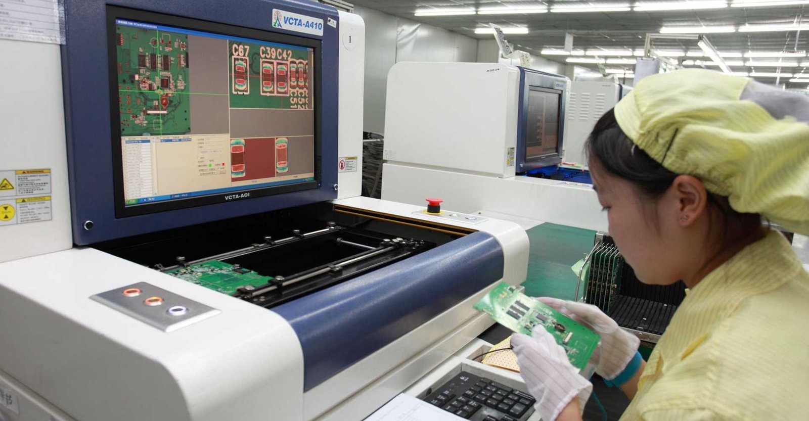 AOI review workstation example | GlobalWellPCB Operator inspecting a circuit board beside an optical-inspection monitor and workstation