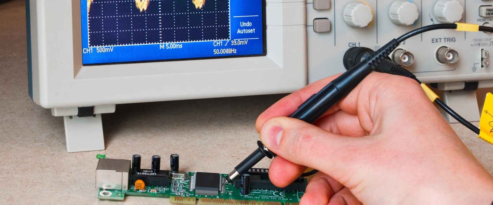 Electronics bench-test example | GlobalWellPCB Hand holding an electrical probe near a populated circuit board and test instrument