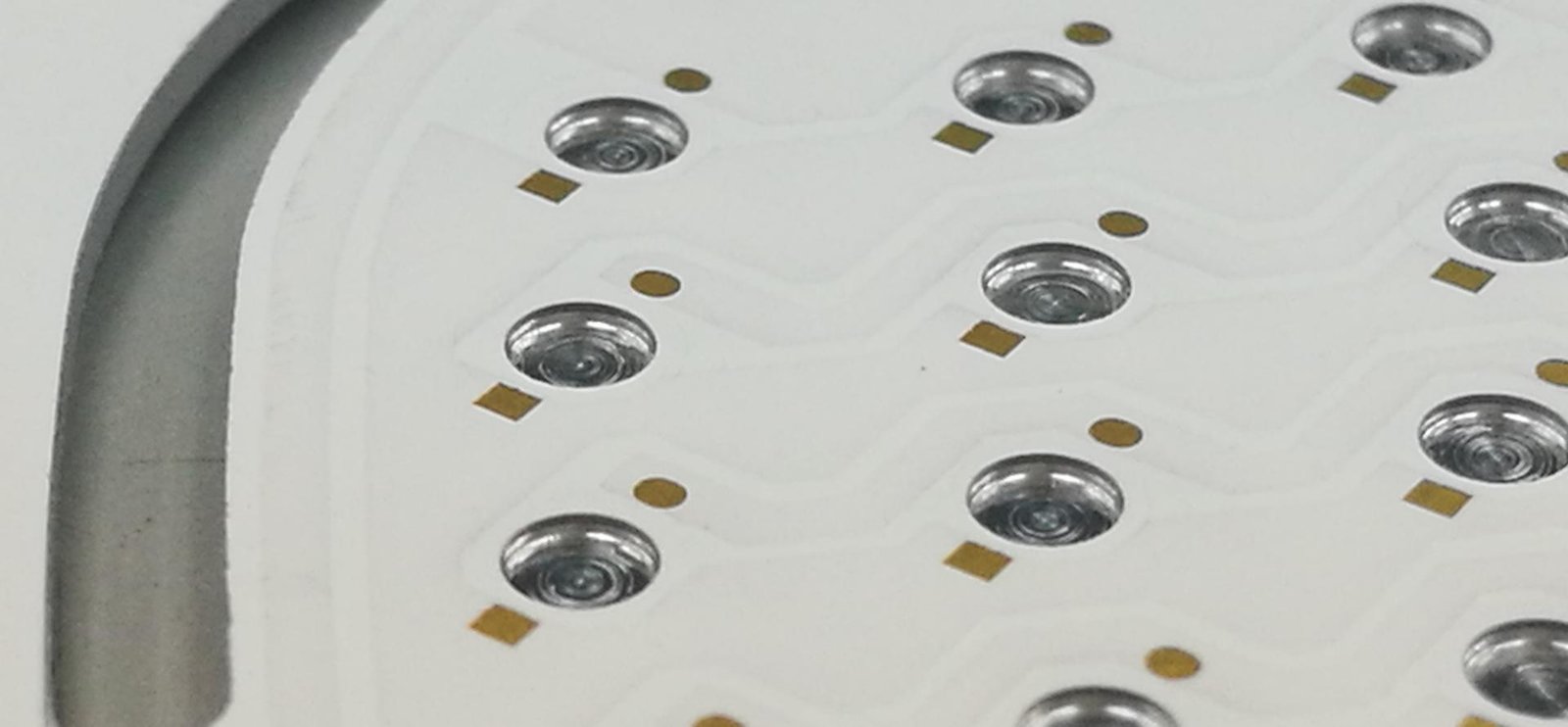 Close-up of mounting holes and component pads on a white circular circuit board