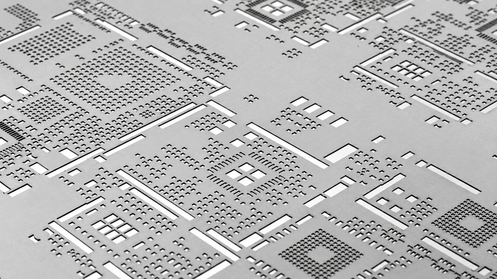 Close-up of a metal PCB stencil with dense arrays of small square and rectangular component apertures